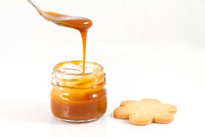 Pouring caramel in a small jar with spoon, horizontal