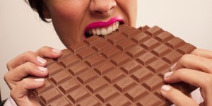 Woman in pink lipstick biting large chocolate bar
